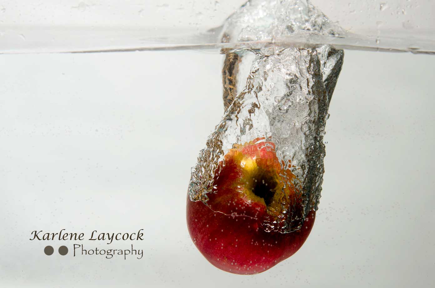 Red Apple plunging in to water on a grey background