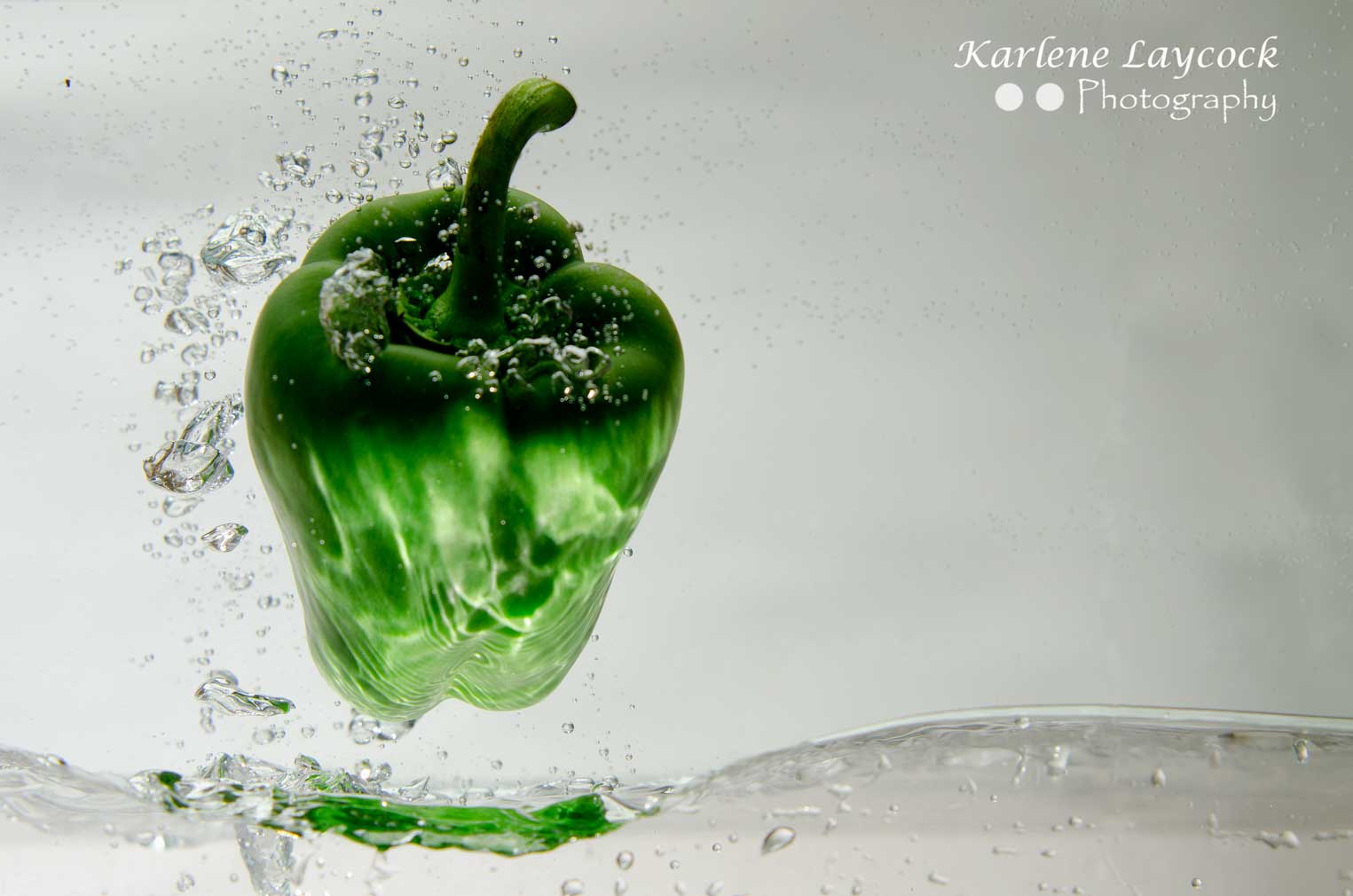 Green Pepper Suspended against a Grey Background with Water Bubbles